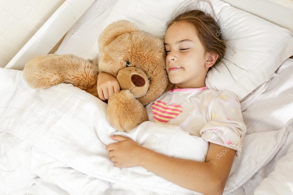 cute girl sleeping and hugging big teddy bear at bed