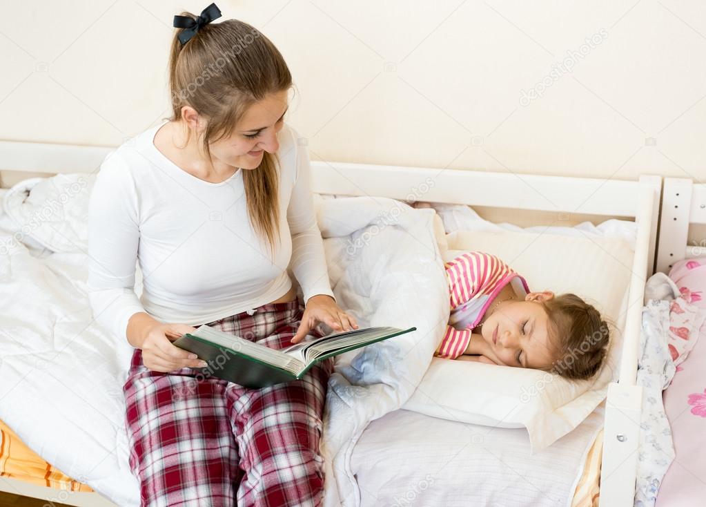 mother sitting on bed next to daughter and reading a story