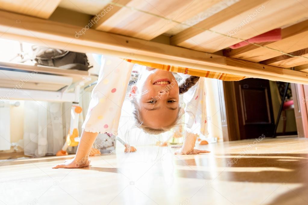 little smiling girl looking under bed