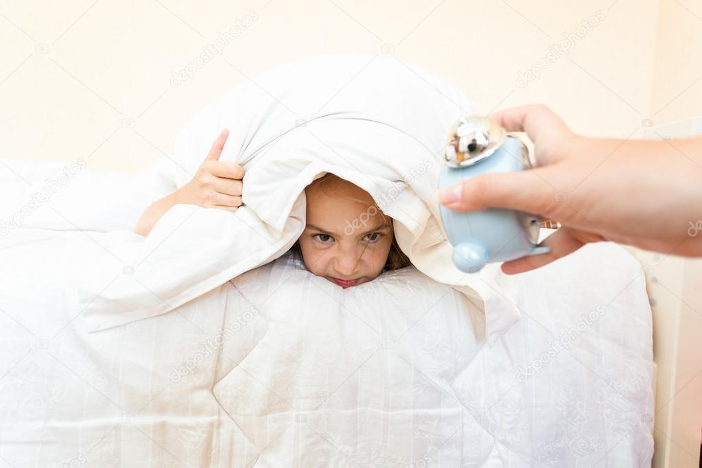 portrait of woman waking up girl with alarm clock at early morni
