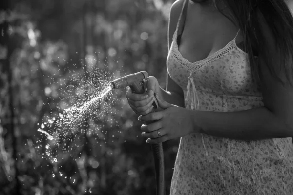Foto monocromática de una joven sosteniendo una manguera de riego en el jardín — Foto de Stock