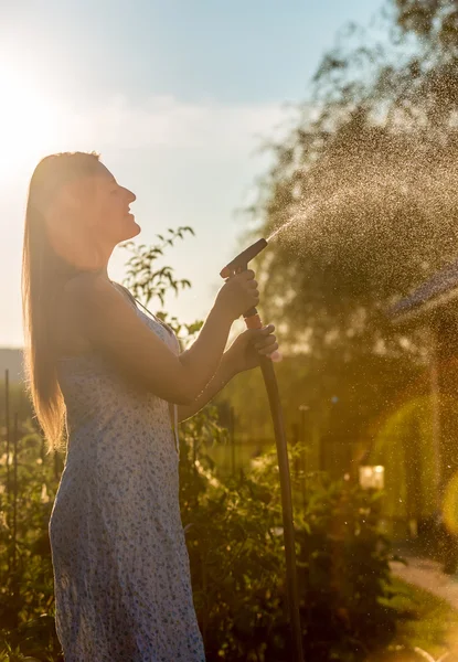 Foto contra o céu da mulher que rega o jardim com mangueira na ensolarada da — Fotografia de Stock