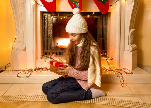 Leuk meisje te kijken naar de gift van Kerstmis bij open haard — Stockfoto