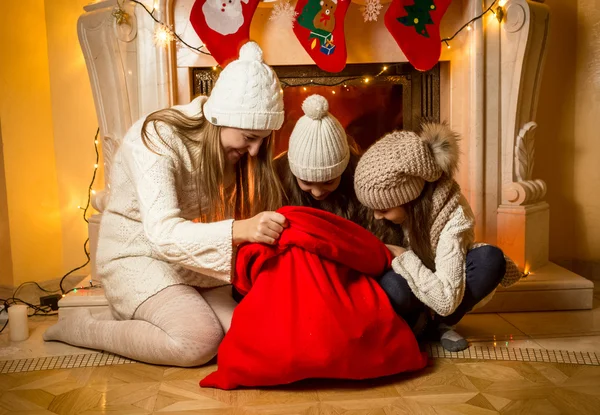 Madre con due figlie che guardano dentro la borsa rossa di Babbo Natale — Foto Stock