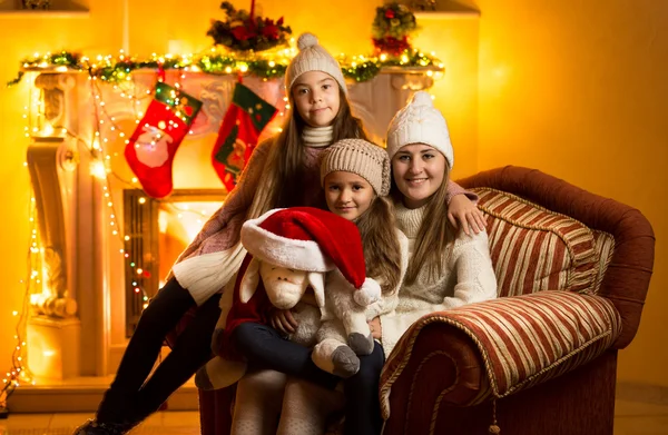 Madre y dos hijas sentadas en el sofá en la chimenea en Christm —  Fotos de Stock