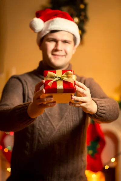 Smiling handsome man in santa hat holding red gift box — Stock Photo, Image