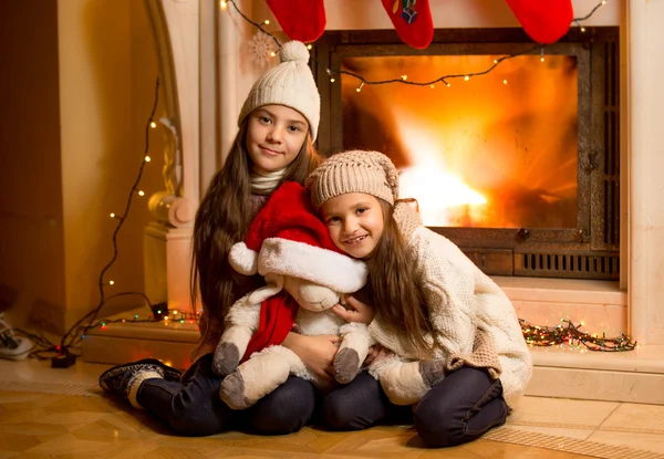 Lächelnde Mädchen in Pullover und Mütze wärmen sich am Kamin auf. — Stockfoto