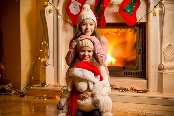 Portrait of two beautiful girls in sweaters sitting at fireplace — Stock Photo, Image