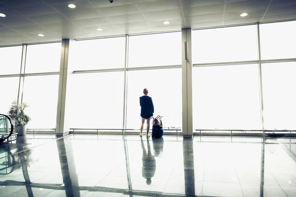 Mulher com mala olhando para grandes janelas no terminal do aeroporto — Fotografia de Stock