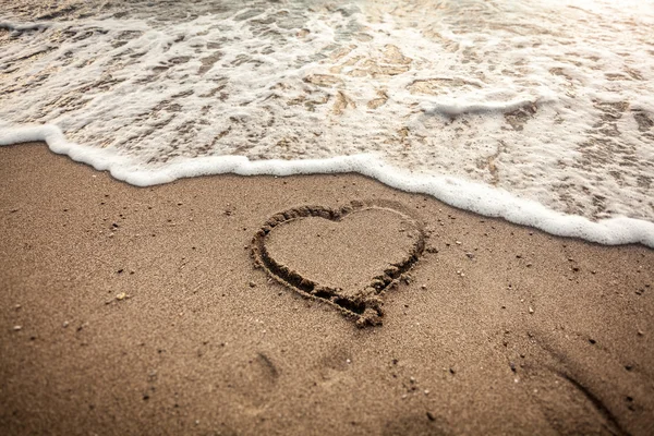 Тонированное фото сердца, нарисованного на песке, омываемом волной — стоковое фото