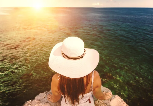 Mujer joven con sombrero blanco mirando el atardecer sobre el mar — Foto de Stock