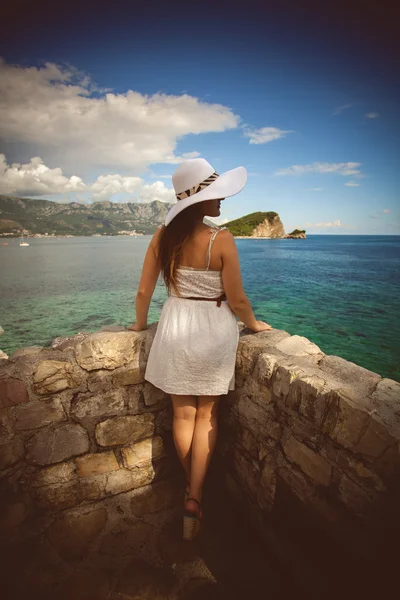 Mladá žena nosí bílý klobouk, při pohledu na daleko ostrov na moři — Stock fotografie