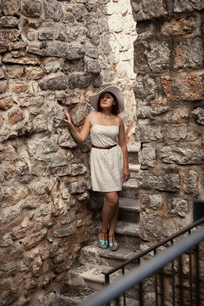 Mujer joven en vestido y sombrero caminando en el antiguo castillo de piedra — Foto de Stock