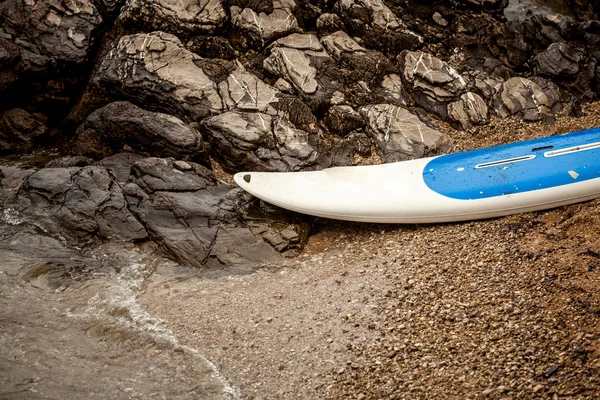 Tabla de surf que se encuentra en la playa de arena en el mar junto a acantilados dentados —  Fotos de Stock