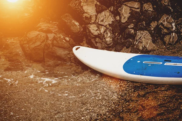 Tabla de surf acostado en la playa de arena al atardecer rayos —  Fotos de Stock