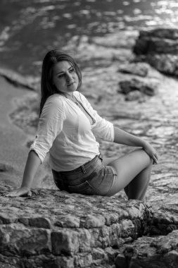 Beyaz gömlekli sahilde büyük kayanın üzerinde rahatlatıcı seksi kadın