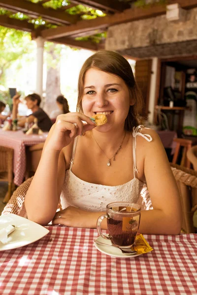 Smiling woman sitting at outdoor cafe and eating cookie — Stock Photo, Image