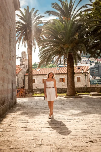 Женщина ходит по улице с древним зданием и высокими пальмами — стоковое фото