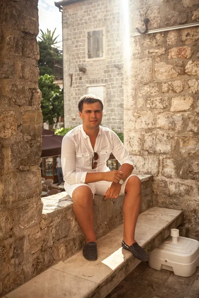 Młody mężczyzna siedzący przy ulicy Starego Miasta w słoneczny dzień — Zdjęcie stockowe