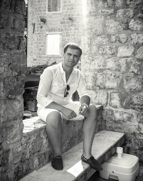 Monochrome photo of handsome man sitting on old street — Stock Photo, Image