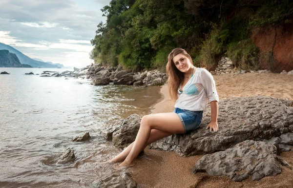 Νεαρή γυναίκα σε άσπρο πουκάμισο χαλάρωση σε βράχο στη θάλασσα ακτή — Φωτογραφία Αρχείου