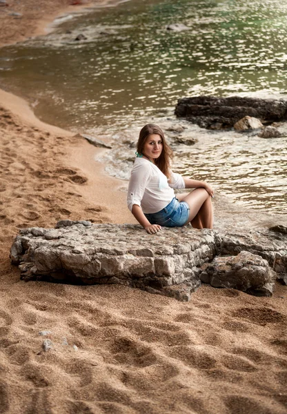 Sexy woman sitting on big rock at sandy sea shore — Stock Photo, Image