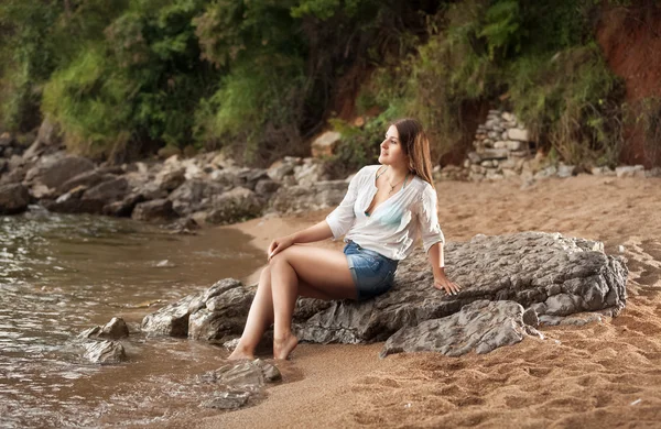 Slim woman wearing white shirt lying on big rock on beach — Stock Photo, Image