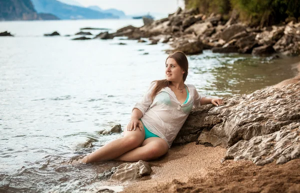 Slim woman in white wet shirt lying on sea shore — Stock Photo, Image