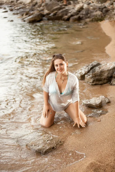 Sexy woman in shirt kneeling on sandy beach — Stock Photo, Image