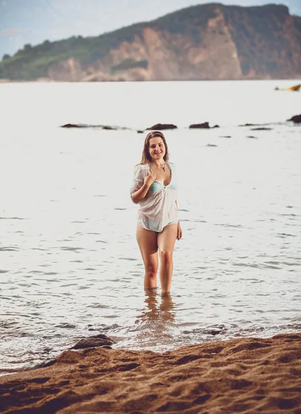 Ung kvinna i vit skjorta gå ut havet på stranden — Stockfoto