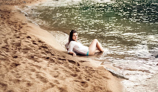 Brunette woman lying on sandy sea shore — Stock Photo, Image