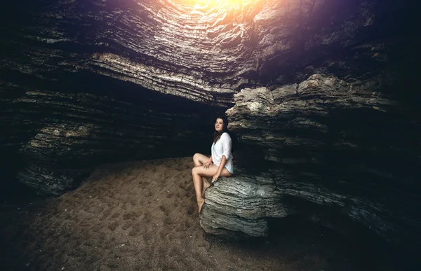 Jeune femme assise sur la falaise à la grotte aux rayons du coucher du soleil — Photo