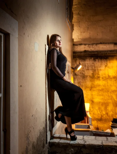 Mulher de vestido longo encostado contra a parede na rua velha à noite — Fotografia de Stock