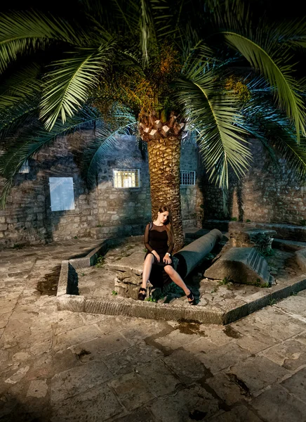 Jeune femme en robe de cocktail noire assise sur la vieille rue à nig — Photo