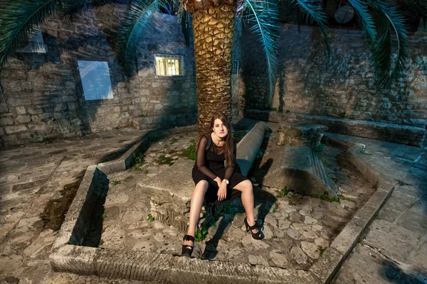 Frau im langen schwarzen Kleid posiert nachts in alten engen Straßen — Stockfoto