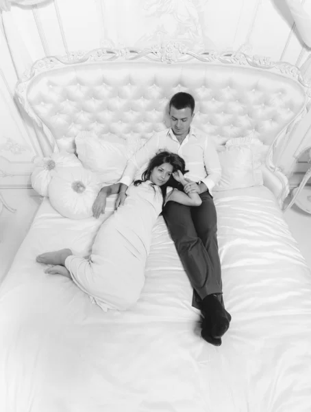 Monochrome photo of romantic couple lying on luxurious white bed — Stock Photo, Image