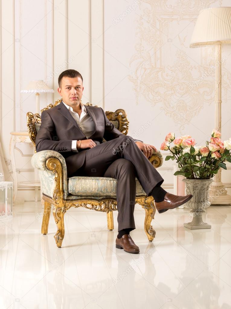 man in black suit sitting in luxurious chair at classic interior