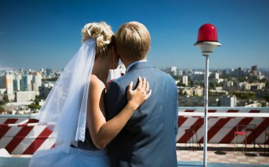 just married couple standing on roof top and looking at the city clipart