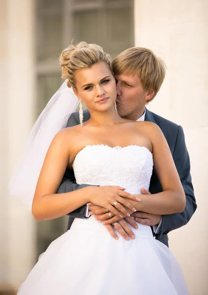 Young groom hugging blonde bride from back on street — Stock Fotó