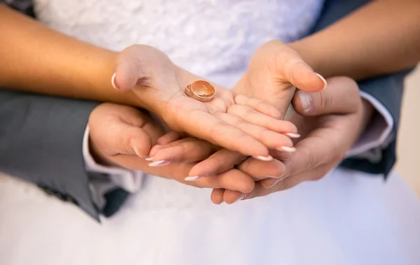 Bride and groom holding golden wedding rings on hands — Stock Photo, Image