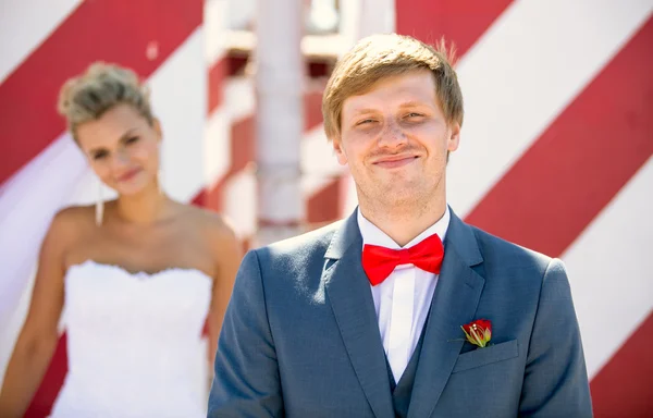 Felice sposo sorridente in posa sulla strada contro la sposa fuori fuoco — Foto Stock