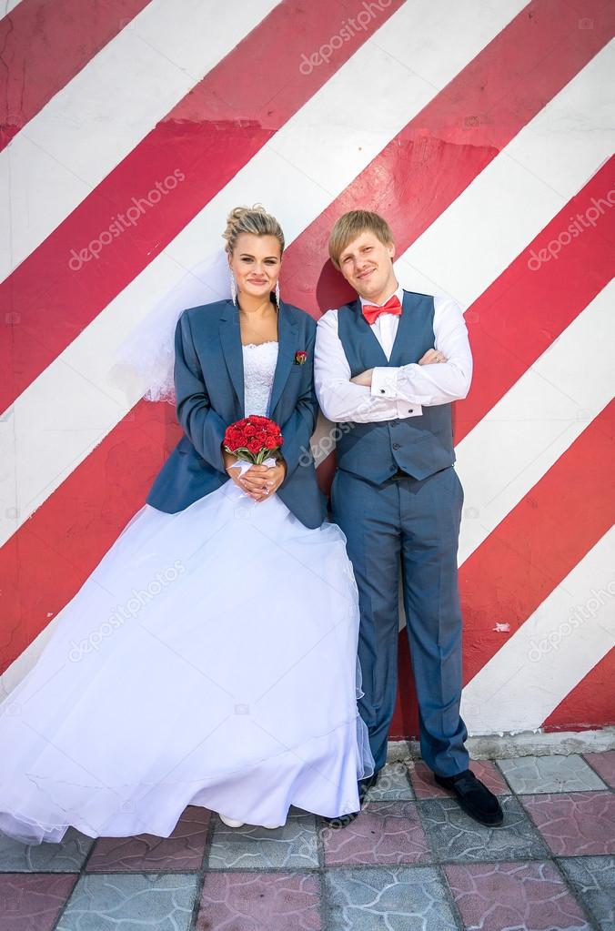 hipster bride and groom posing against red striped wall 