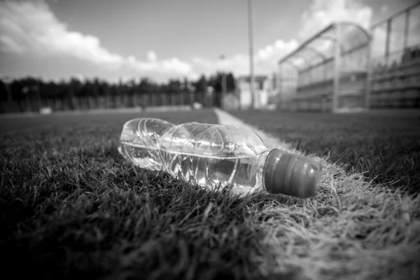 Monochrome shot of bottle of water lying on soccer field — Stock Photo, Image