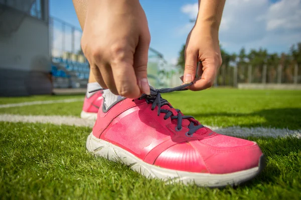 Frau schnürt rosa Turnschuhe auf Fußballplatz — Stockfoto