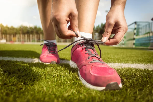 Woman tying laces on sneakers on grass field — Stock Photo, Image
