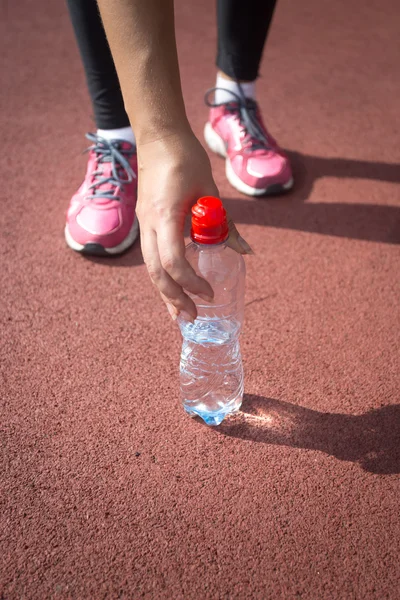 Sporty woman taking bottle of water from running track — Stock Photo, Image