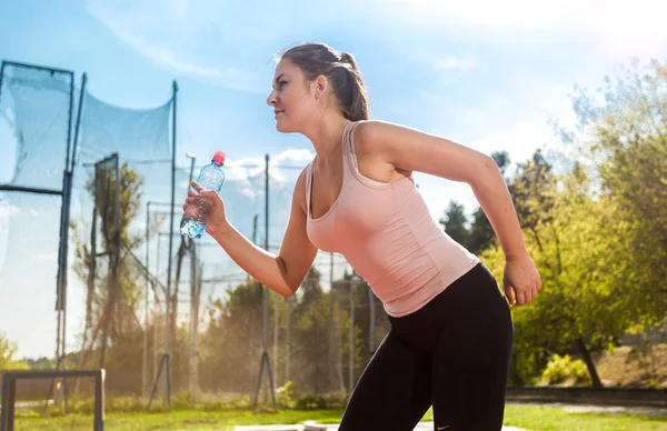 Laufende junge Frau mit Wasserflasche im Stadion — Stockfoto