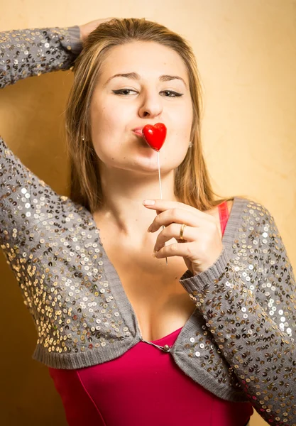 Cute stylish woman holding red heart on stick at lips — Stock Photo, Image