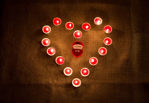 Anillo de oro en la caja acostado en medio de la forma del corazón de las velas — Foto de Stock