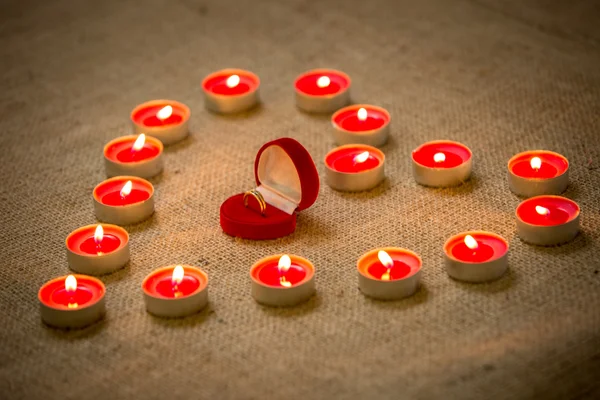 Anillo de oro en la caja que miente dentro de la forma del corazón hecha de velas — Foto de Stock